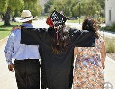 a man and woman walking down a sidewalk with their arms around each other wearing graduation caps