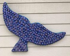 a blue fish made out of plastic bottles on the side of a building with white siding