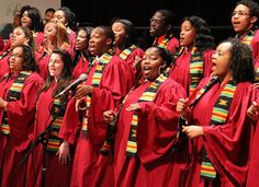 a group of women singing on stage with microphones in their hands and wearing red gowns