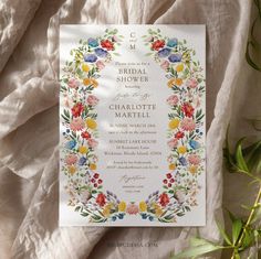 a wedding card with flowers and leaves on the front, sitting next to a plant