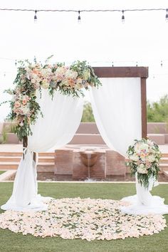 an outdoor wedding setup with flowers on the ground and drapes in the air,