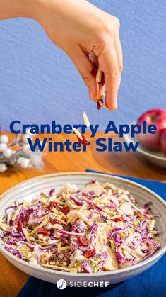 a person is picking up an apple from a bowl filled with coleslaw and cranberries