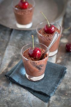 two desserts with cherries and chocolate pudding in small cups on a table top