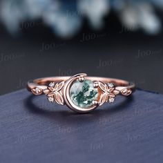 a ring with an oval cut green stone in the center and leaves around it, on top of a blue surface