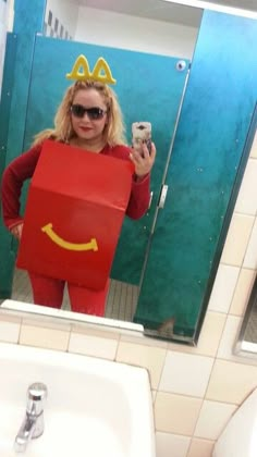 a woman taking a selfie in a bathroom mirror with a box shaped like a smiling face