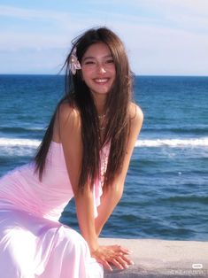 a woman in a pink dress sitting on a ledge near the ocean