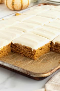 a cake with white frosting sitting on top of a wooden cutting board next to some pumpkins