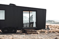 a man standing in front of a black tiny house