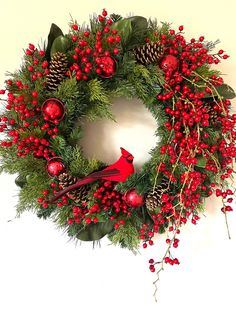 a christmas wreath with red berries, pine cones and a cardinal bird on the front