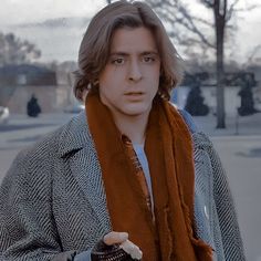 a man with long hair wearing a coat and scarf