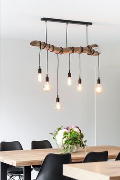 a wooden table with black chairs and light bulbs hanging from it's centerpiece