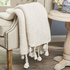 a white knitted blanket sitting on top of a chair next to a wooden table