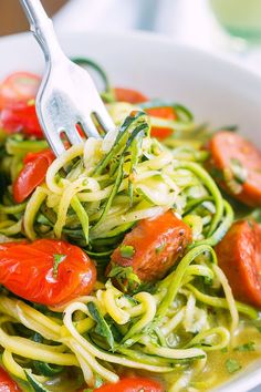 a white bowl filled with zucchini, tomatoes and pesto noodles on top of a table