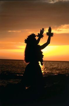 the silhouette of a woman with her hands in the air, standing on a beach at sunset