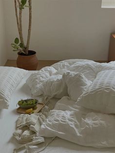 an unmade bed with white sheets, pillows and a bowl of fruit on it