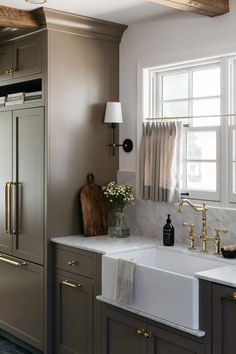 a kitchen with gray cabinets and white counter tops, gold faucets and brass pulls