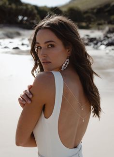 a woman standing on the beach wearing a white dress and pearls in her earrings