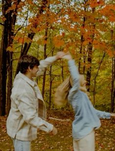 a man and woman dancing in the woods with autumn leaves on the ground behind them