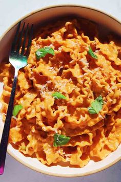 a white bowl filled with pasta and sauce on top of a table next to a fork