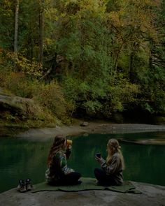 two young women sitting on the edge of a river