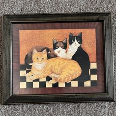 three cats are sitting on a checkerboard floor in front of a framed painting