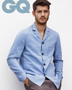 a man standing in front of a white wall wearing a blue shirt and gray pants