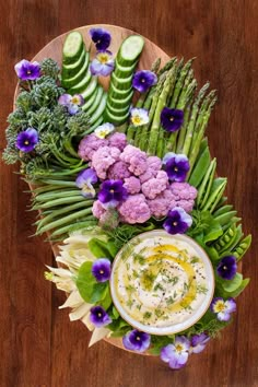 a plate filled with different types of food on top of a wooden table next to flowers and cucumbers