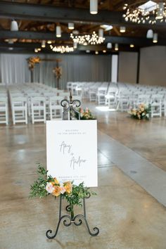 a sign that is sitting on top of a metal stand with flowers and greenery