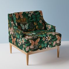 an upholstered chair with flowers and butterflies on it, against a blue wall