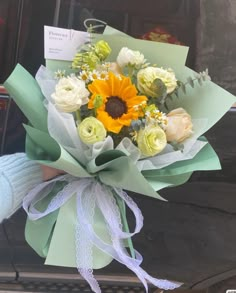 a bouquet of sunflowers and white roses in someone's hand outside their car