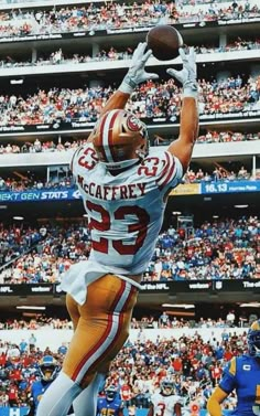 a football player jumping up into the air to catch a ball in front of an arena full of people