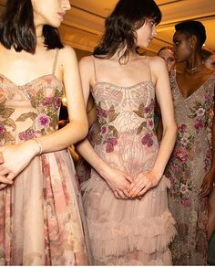 three women in dresses standing next to each other at a fashion show with others looking on