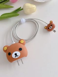 two brown bears are plugged into a charger on a white table next to tulips