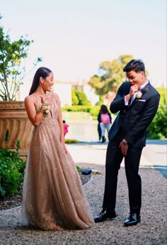 a man standing next to a woman in a gold dress on top of a gravel road