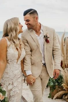 a bride and groom holding hands on the beach