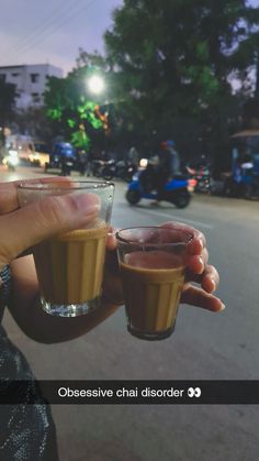 a woman holding two glasses filled with liquid on the side of a road at night