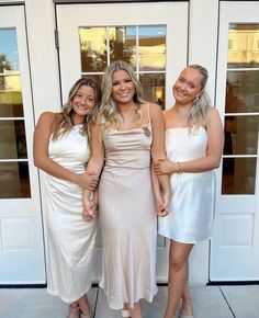 three beautiful women standing next to each other in front of a white door wearing dresses