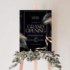 a black and gold grand opening sign on top of a easel with greenery