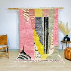 a colorful rug is hanging on the wall next to a wooden chair and table with a vase