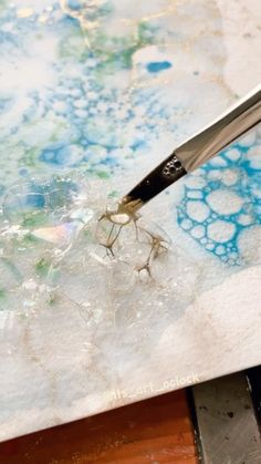 a pair of scissors cutting through some ice on a piece of paper with blue and green paint