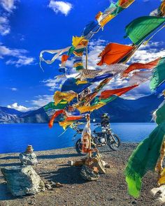 there are many colorful flags flying in the wind next to a motorbike and mountain lake