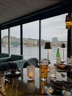 a table with glasses and plates on it in front of a window overlooking the water