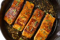 four salmon fillets in a skillet with herbs and seasoning on the side