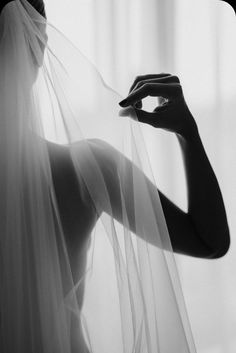 a black and white photo of a woman holding a veil over her face with one hand