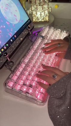 a woman typing on a pink keyboard with diamond nails and ring bracelets in front of a computer screen