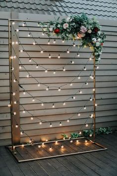 a wedding arch decorated with flowers and greenery is lit up by fairy lights on the side