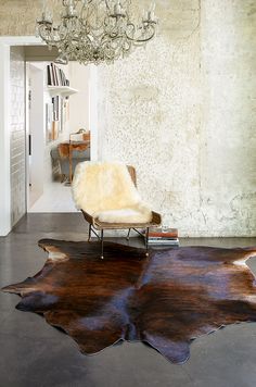 a living room area with a chair, chandelier and cowhide rug on the floor