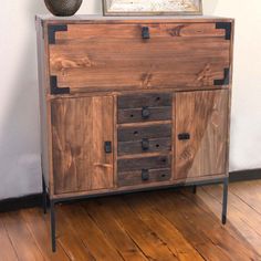 a wooden cabinet sitting on top of a hard wood floor next to a vase with flowers