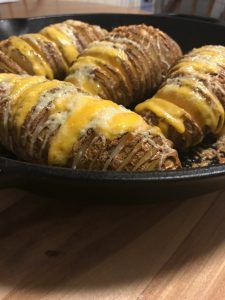 baked potatoes in a skillet with cheese drizzled over them on a wooden table