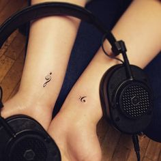 two people with headphones on their feet and one has a small music note tattoo